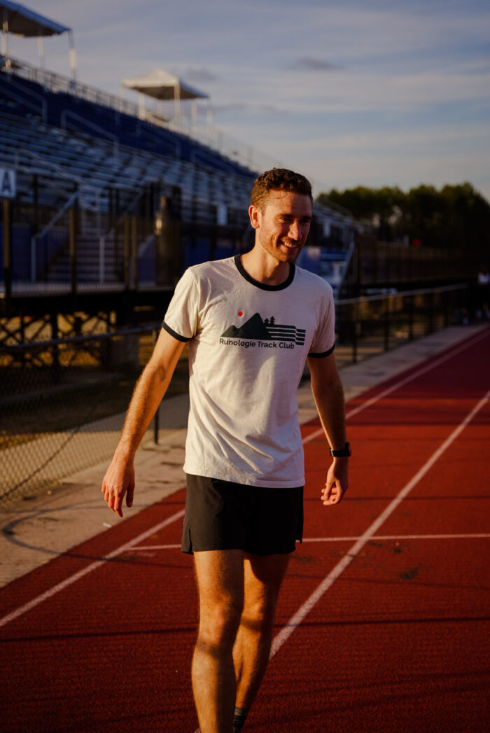 Person standing on the track smiling in a Runologie Track Club shirt 