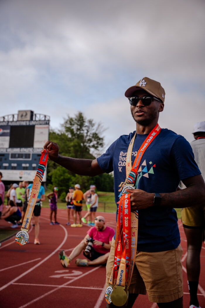 person standing handing out medals at Runologie Track Club 5k.