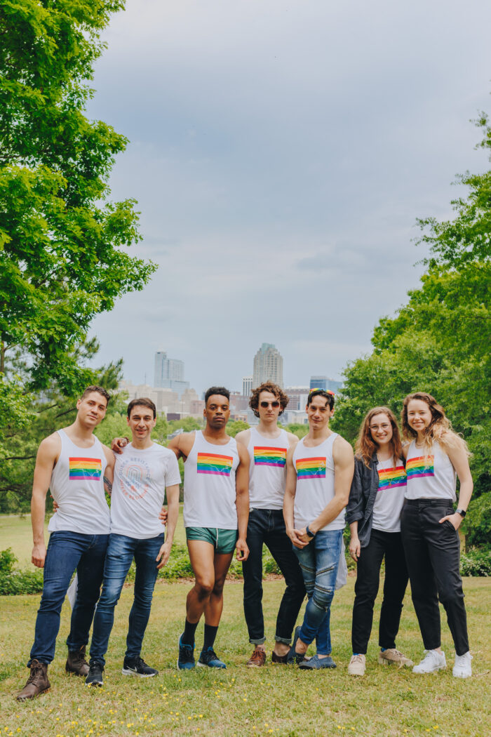 7 people posing with pride flags on their shirts. 