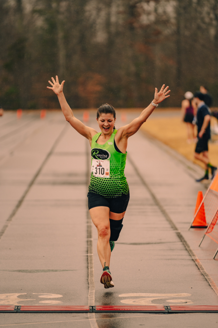Woman celebrates as she crosses the finish line. At Raleigh Half by Sir Walter Running. 