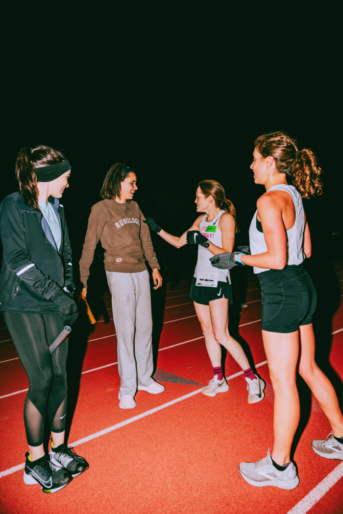 Four women talking and smiling on a track after a run. 