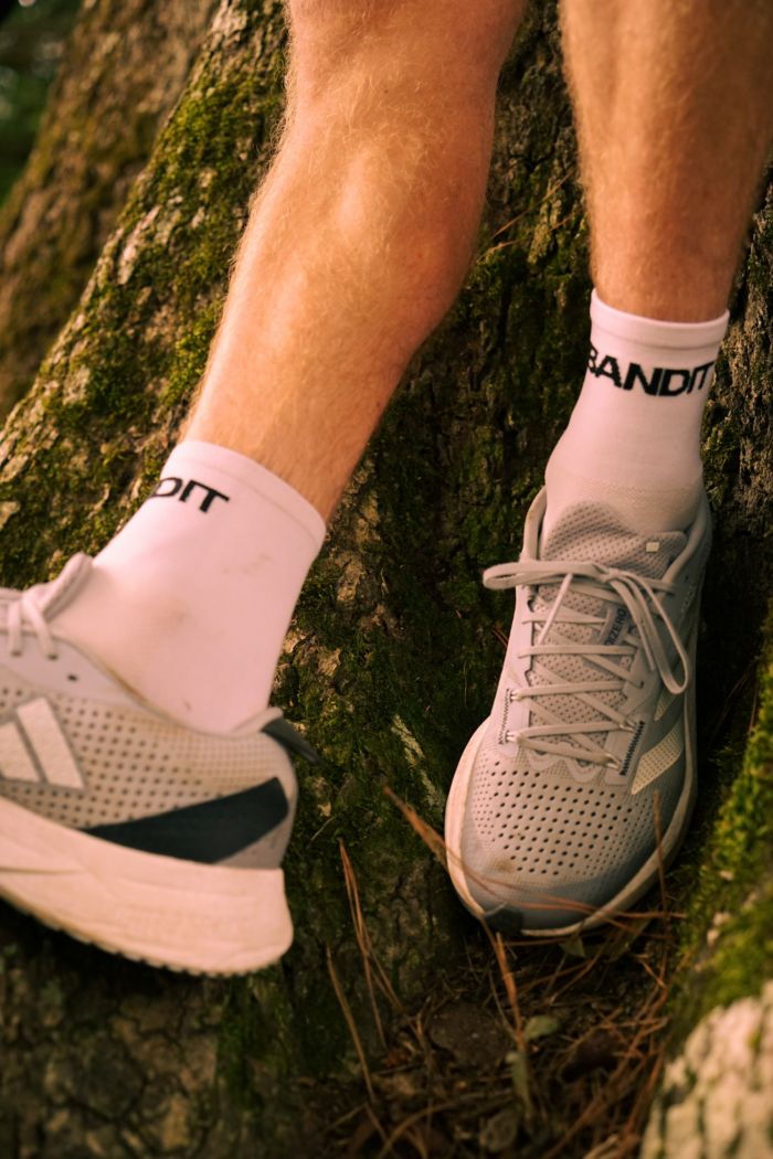 Feet in Bandit running socks in Adidas shoes with tree bark background. 